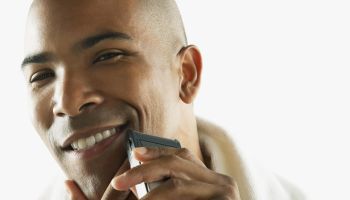 African American man shaving face with electric razor
