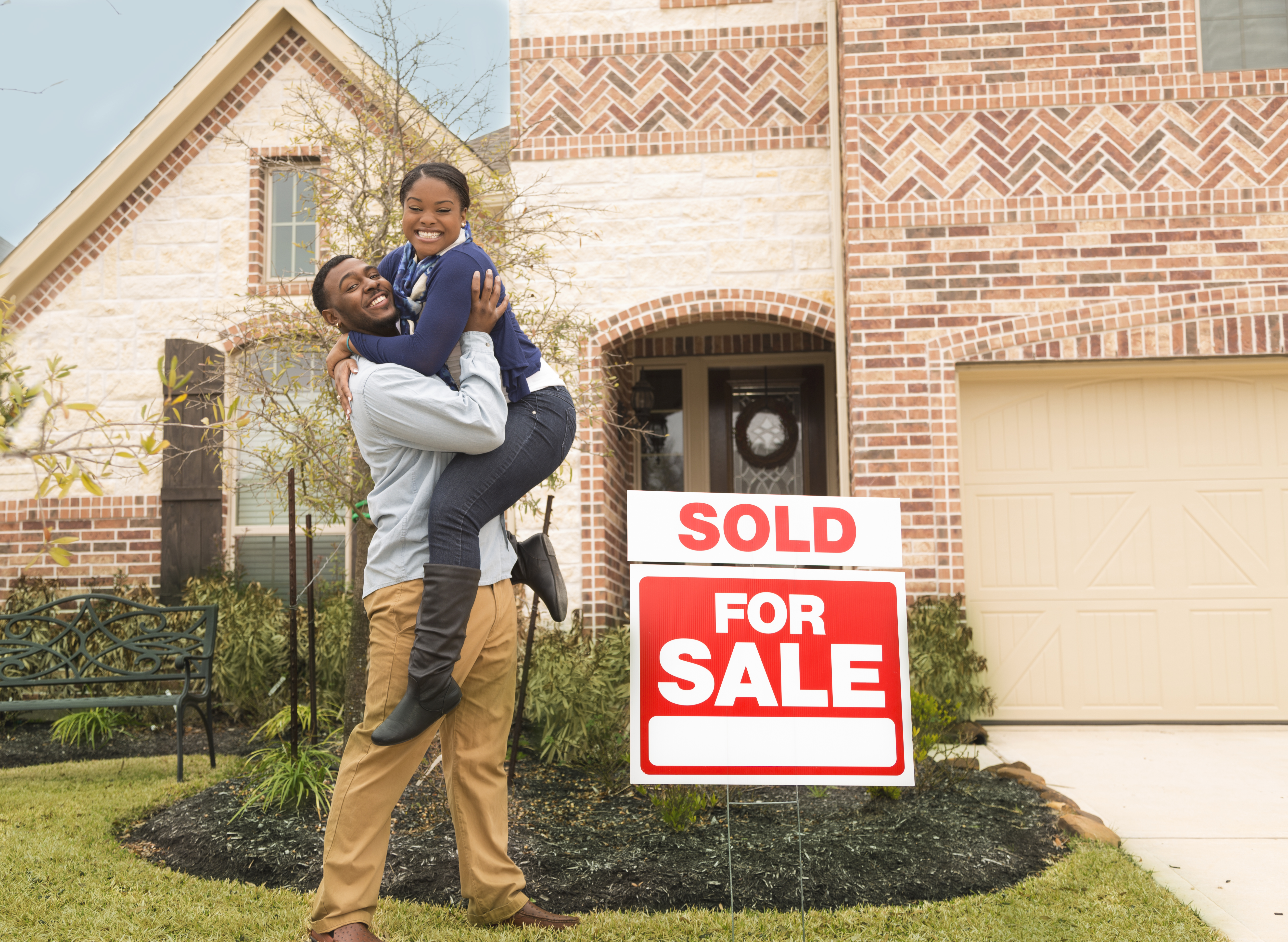 Excited couple jumps for joy in front of first home.