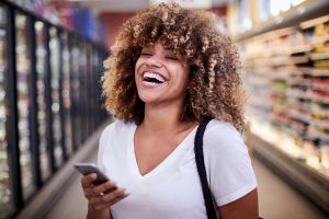 Black woman holding cell phone laughing in grocery store