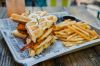 Fried Chicken and bacon waffle sandwich with french fries in an outdoor restaurant setting.