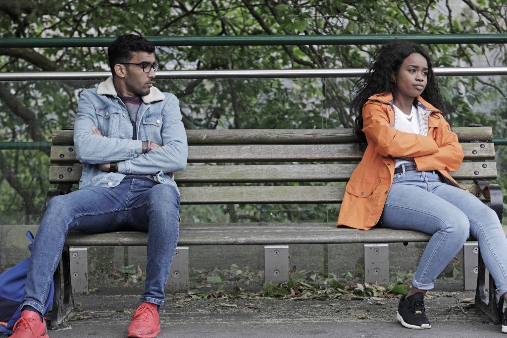 Man and woman sat at opposite ends of bench, not happy