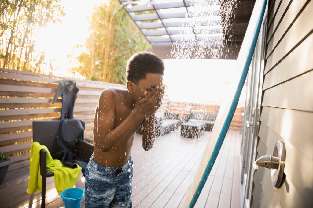 African American boy in swim trunks using beach house shower on deck