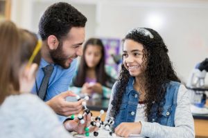 Cheerful teenage girl laughs with STEM teacher in class