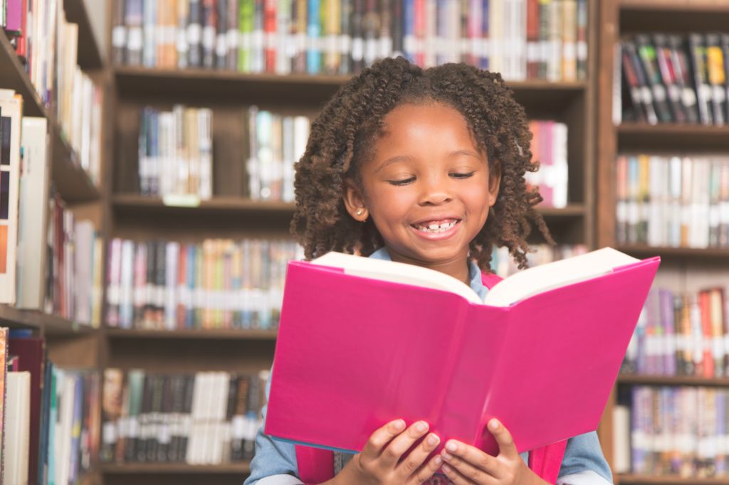 African descent little girl in school library reading book.