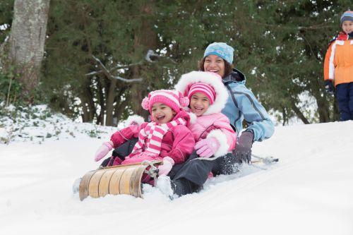 Mother and daughters sledding on snowy hill outdoors