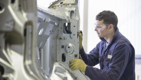 Apprentice wearing boiler suit inspecting car body parts in car plant