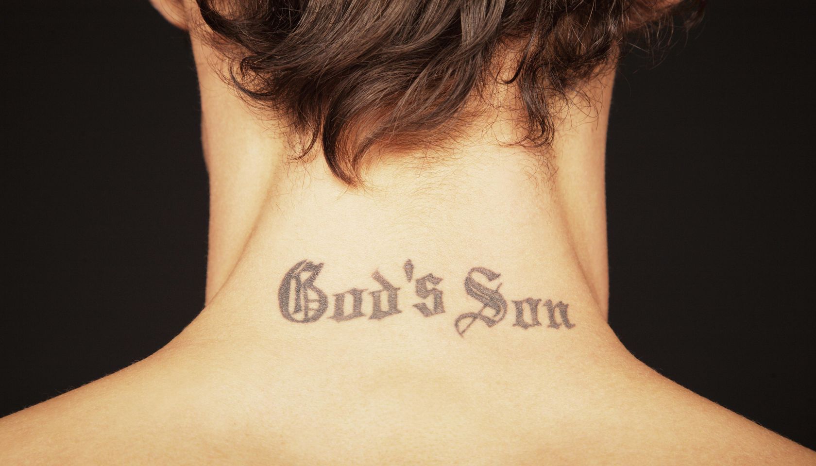Man with tattoo on neck reading 'God's son', close-up, rear view