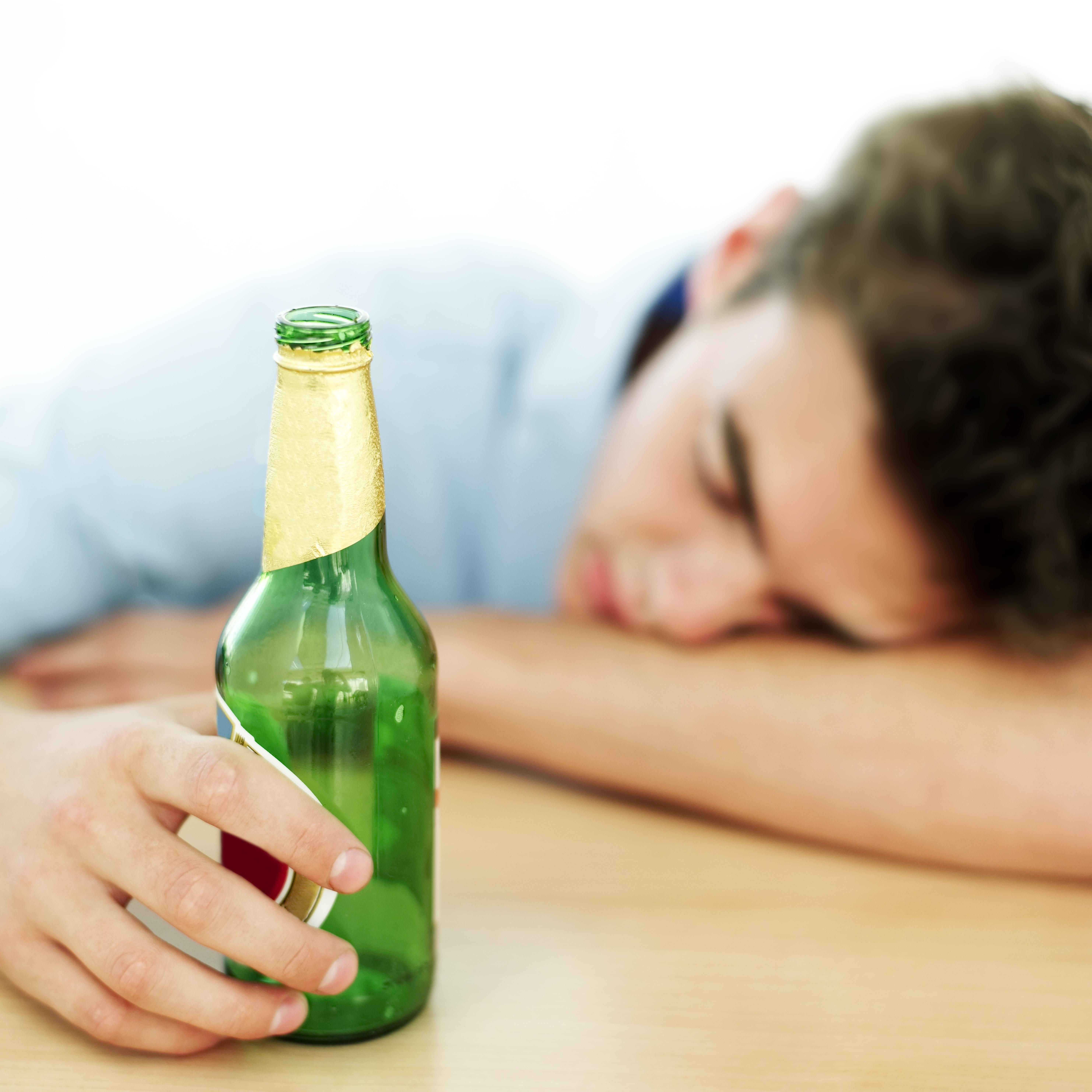 young man asleep on a table while holding an empty beer bottle