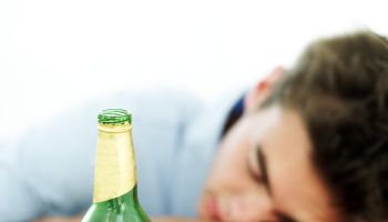 young man asleep on a table while holding an empty beer bottle