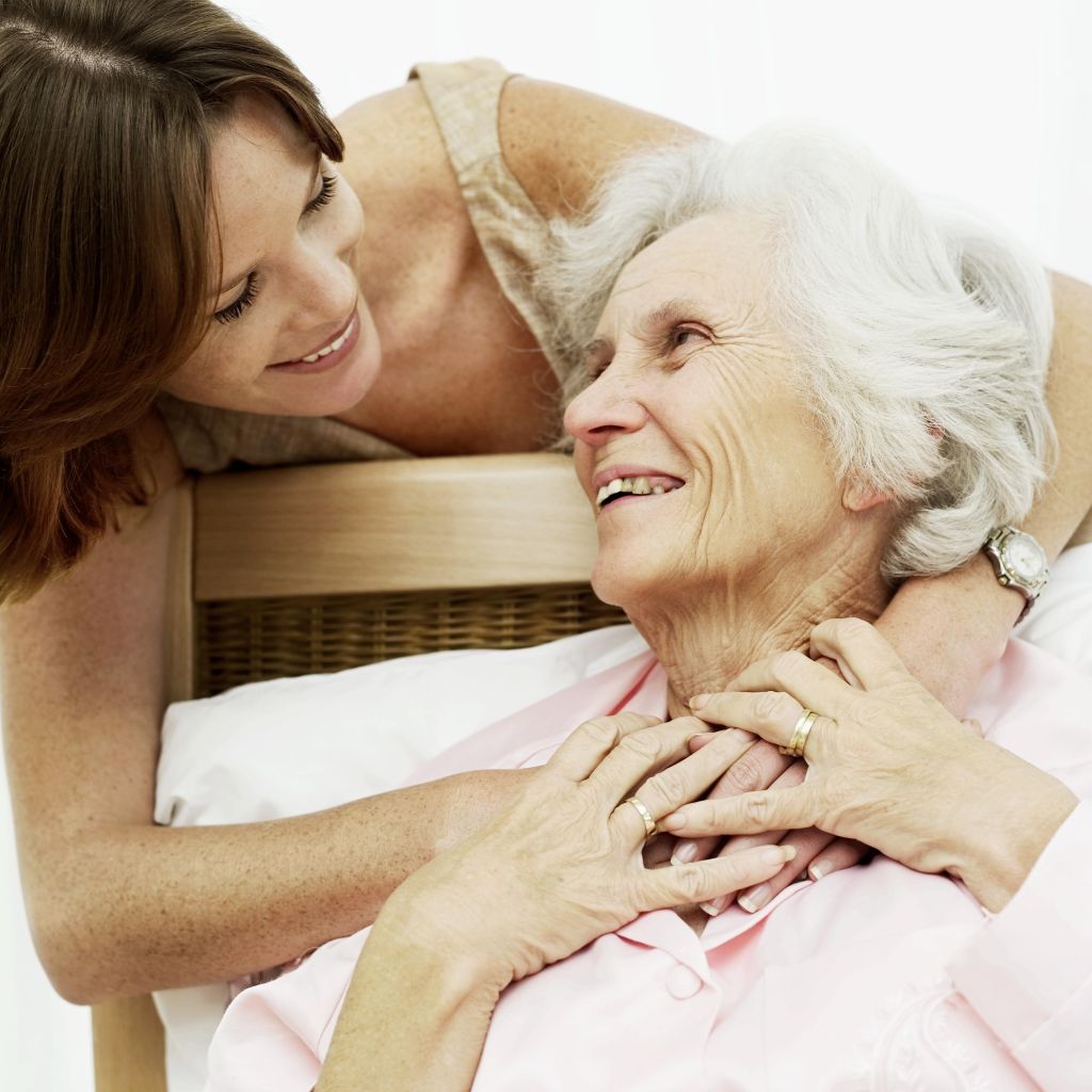 woman smiling and holding an old woman in bed