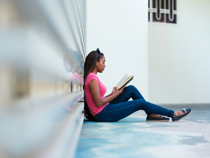Young woman reading a book outside a campus building