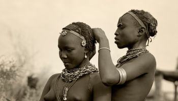 Ethiopia, Omo Delta. A Dassanech girl braids her sister's hair at her village in the Omo Delta