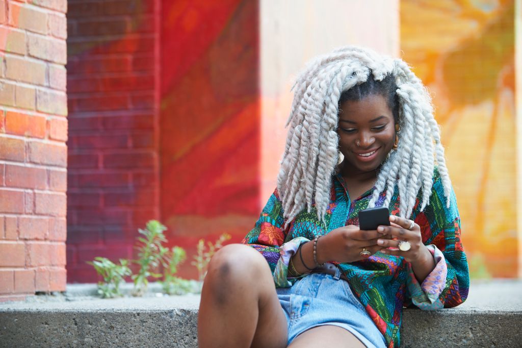 Smiling Black woman texting on cell phone