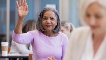 Attractive mature African American woman raises hand in class