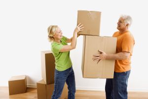 Middle-aged man holding cardboard moving boxes while woman places one on stack.