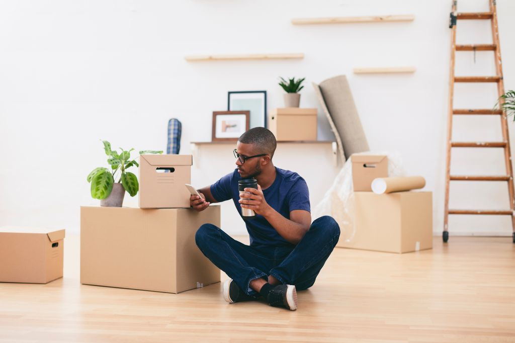 Young man sitting beside cardboard boxes having a coffee break