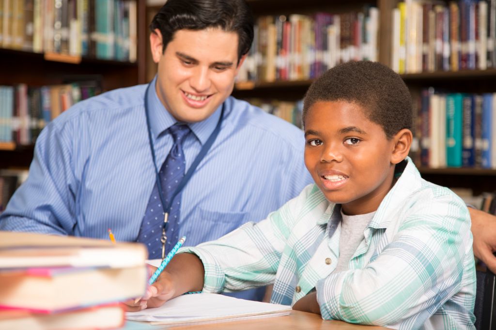 Teacher, mentor helps elementary-age schoolboy with homework.