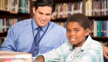 Teacher, mentor helps elementary-age schoolboy with homework.