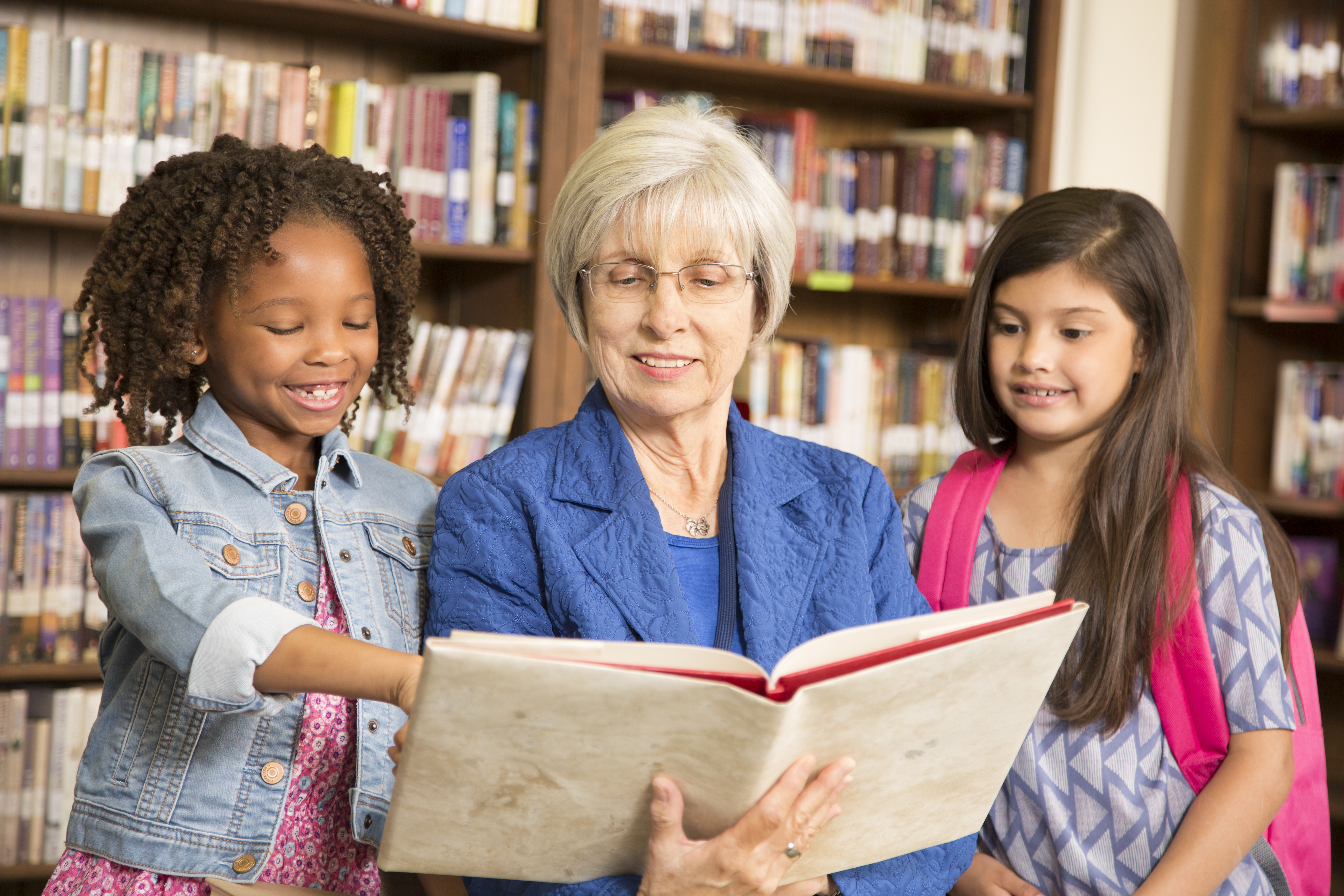 Teacher, librarian reads book to elementary students in library or classroom.