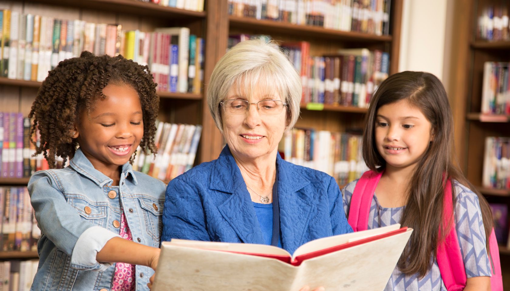 Teacher, librarian reads book to elementary students in library or classroom.