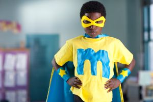 African American boy wearing superhero costume in classroom