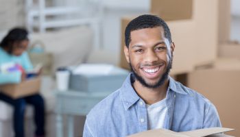Young man smiles for camera while holding moving box