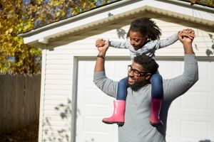 Mature man carrying daughter on shoulders by residential garage