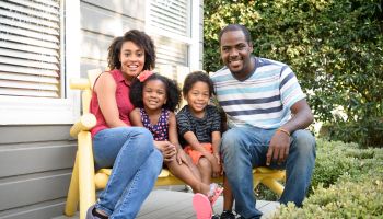 Young African American family sitting on bench outside house