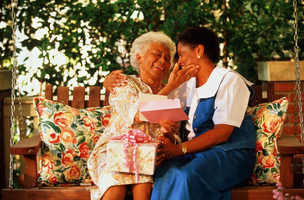 Mature woman giving elderly mother gift and card on porch swing