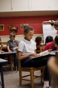 Girl reading book in classroom, children in background