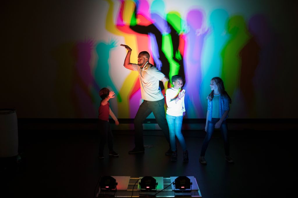 Scientist and children casting multicolor shadows on projection screen in science center theater