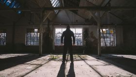 Adult man standing inside some large, dark, spooky,abandoned building illuminated with sunlight through window