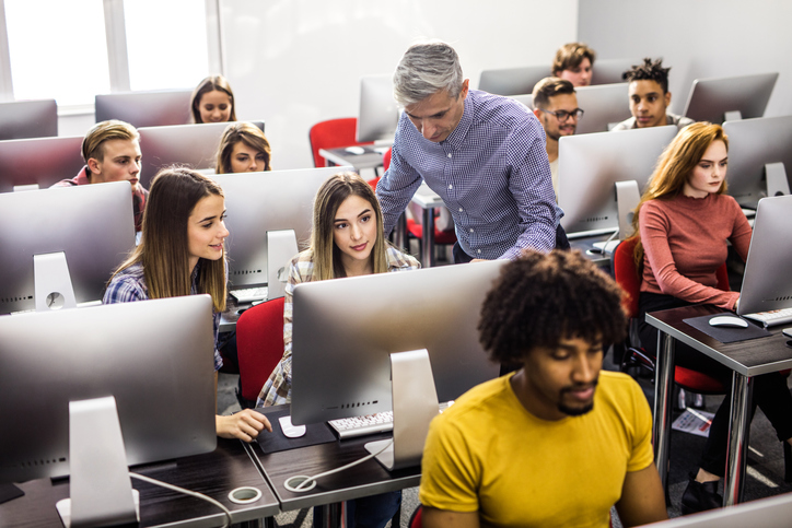 Mid adult professor assisting young students during a class at computer lab.