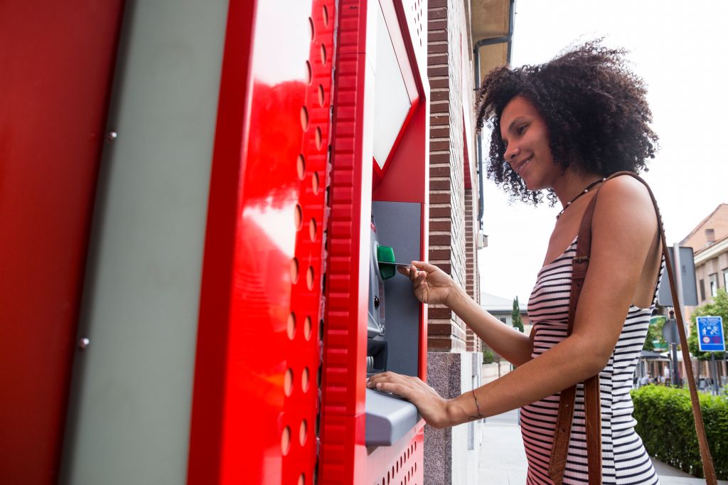 Smiling woman pushing credit card at cash dispenser