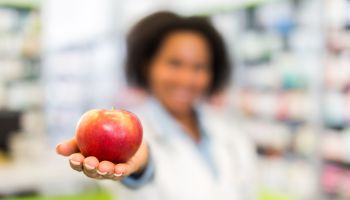 African American pharmacist holding apple in a pharmacy.