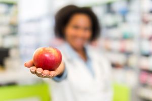 African American pharmacist holding apple in a pharmacy.