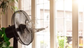 Electric cooling fan with blowing ribbons in front of window on hot summer day