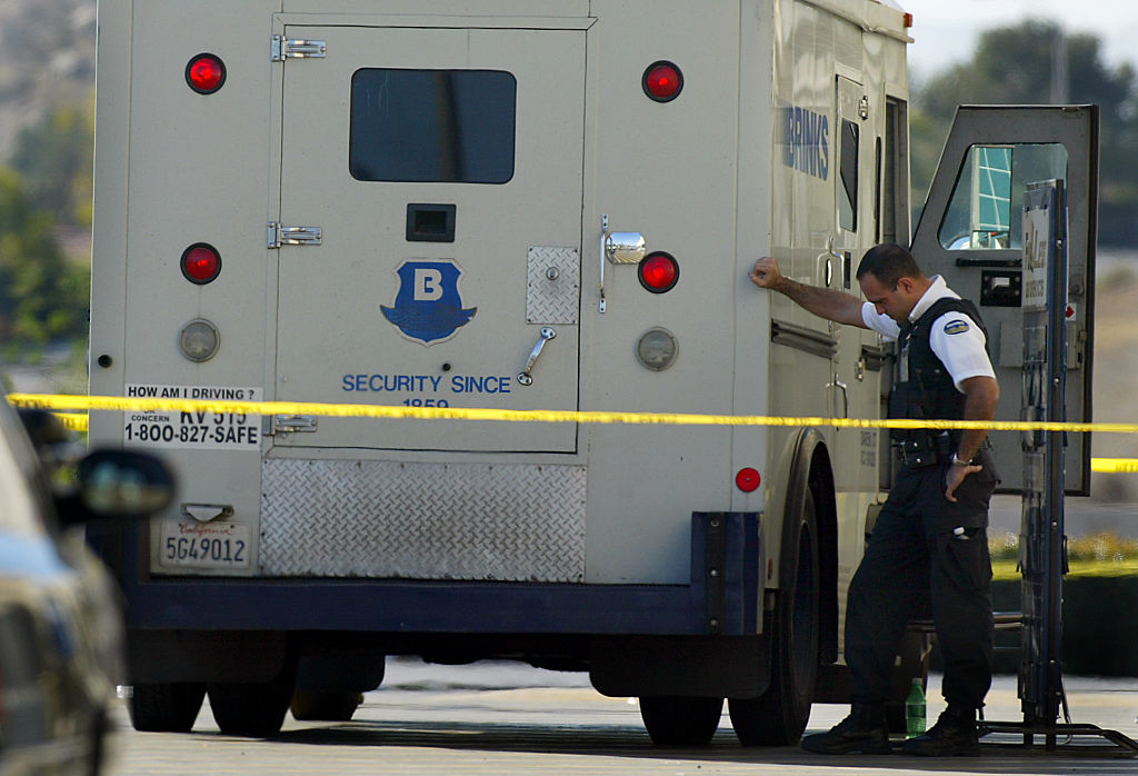 A Brinks security gaurd gathers his thoughts leaning on the armored truck outside the entrance to th